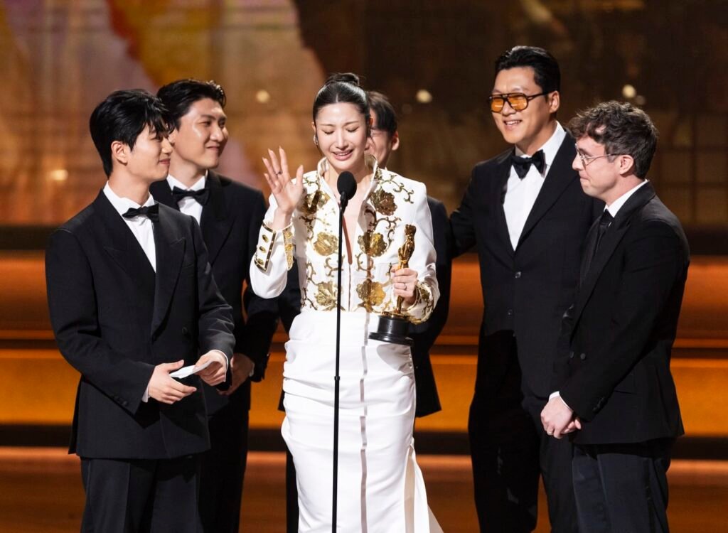 Equipo de la película K-pop Demon Hunters celebrando su victoria a mejor canción original sosteniendo la estatuilla del Óscar con una expresión de felicidad