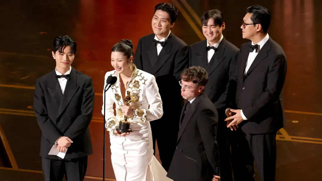 Equipo de la película K-pop Demon Hunters celebrando su victoria a mejor canción original sosteniendo la estatuilla del Óscar con una expresión de felicidad