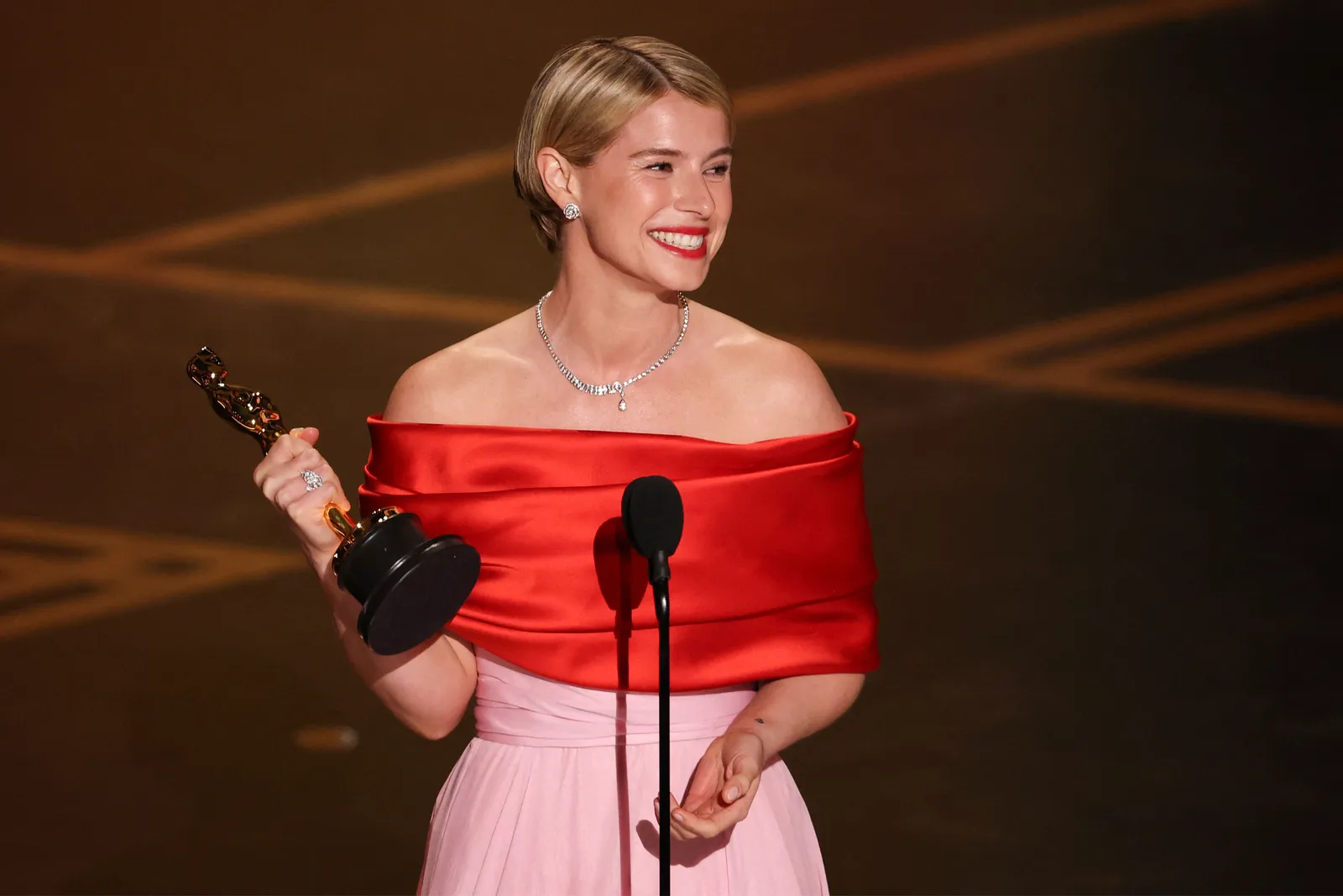 Jessie Buckley en el escenario de los Oscars, sosteniendo la estatuilla y hablando frente a un micrófono.  