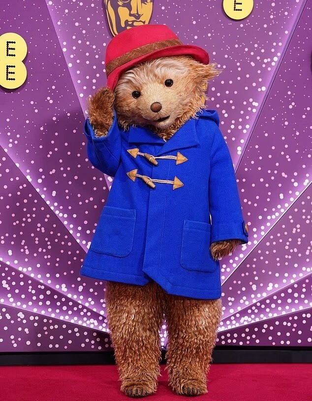 El oso Paddington posando en la alfombra roja de los BAFTA frente a un fondo púrpura.