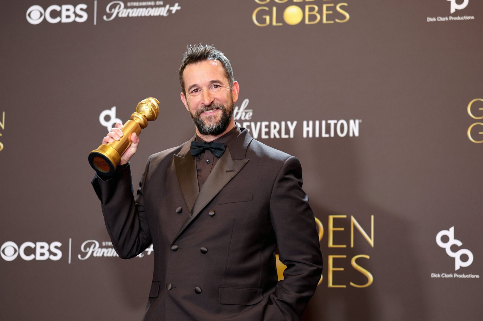 Noah Wyle en la alfombra de los Golden Globes 2026 sonriendo y  sosteniendo su premio obtenido durante la ceremonia.
