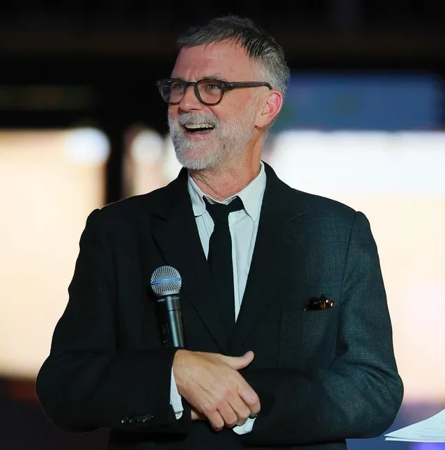 Paul Thomas Anderson en el escenario de los Óscar 2026, con cabello canoso y barba, sonríe ampliamente mientras se dirige al público